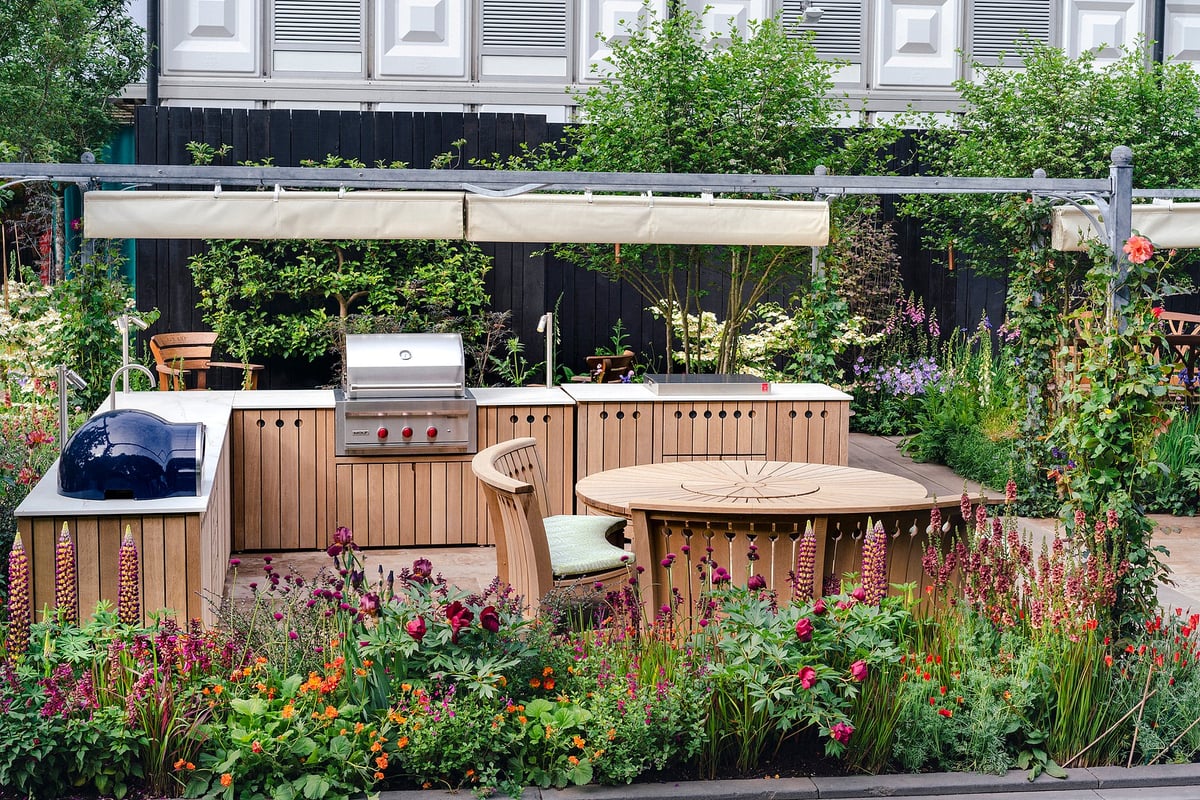Garden with wooden furniture, an outdoor kitchen including a large BBQ grill and a pizza oven
